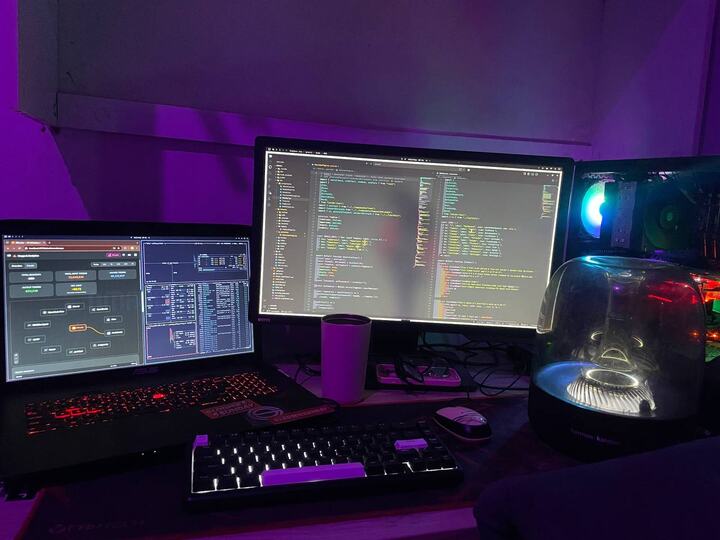 Purple-lit desk setup with monitor, laptop, and mechanical keyboard